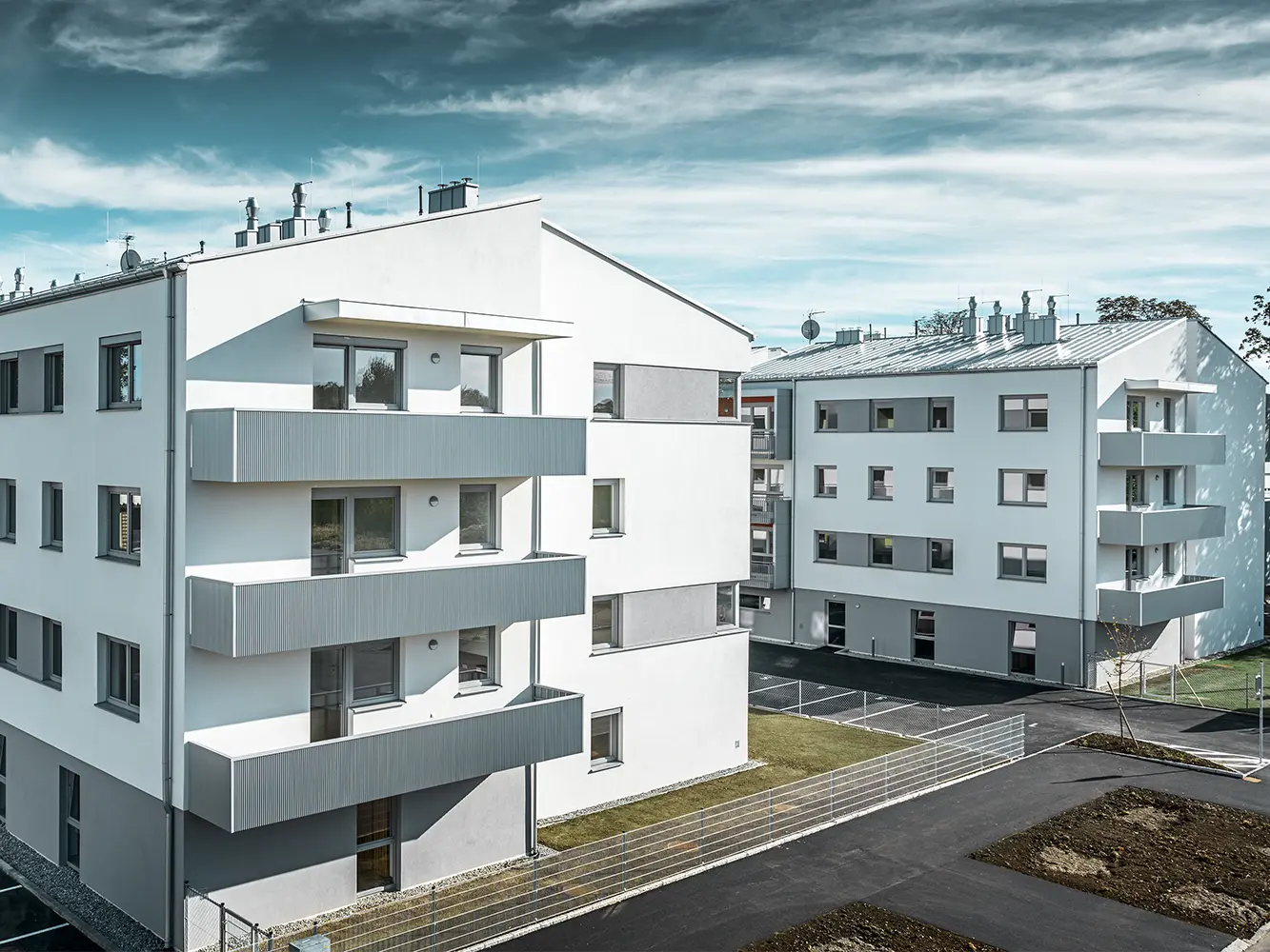 Complex rezidențial modern cu fațadă albă și balcon cu profil PREFA zimțat, de culoare argintiu metalizat