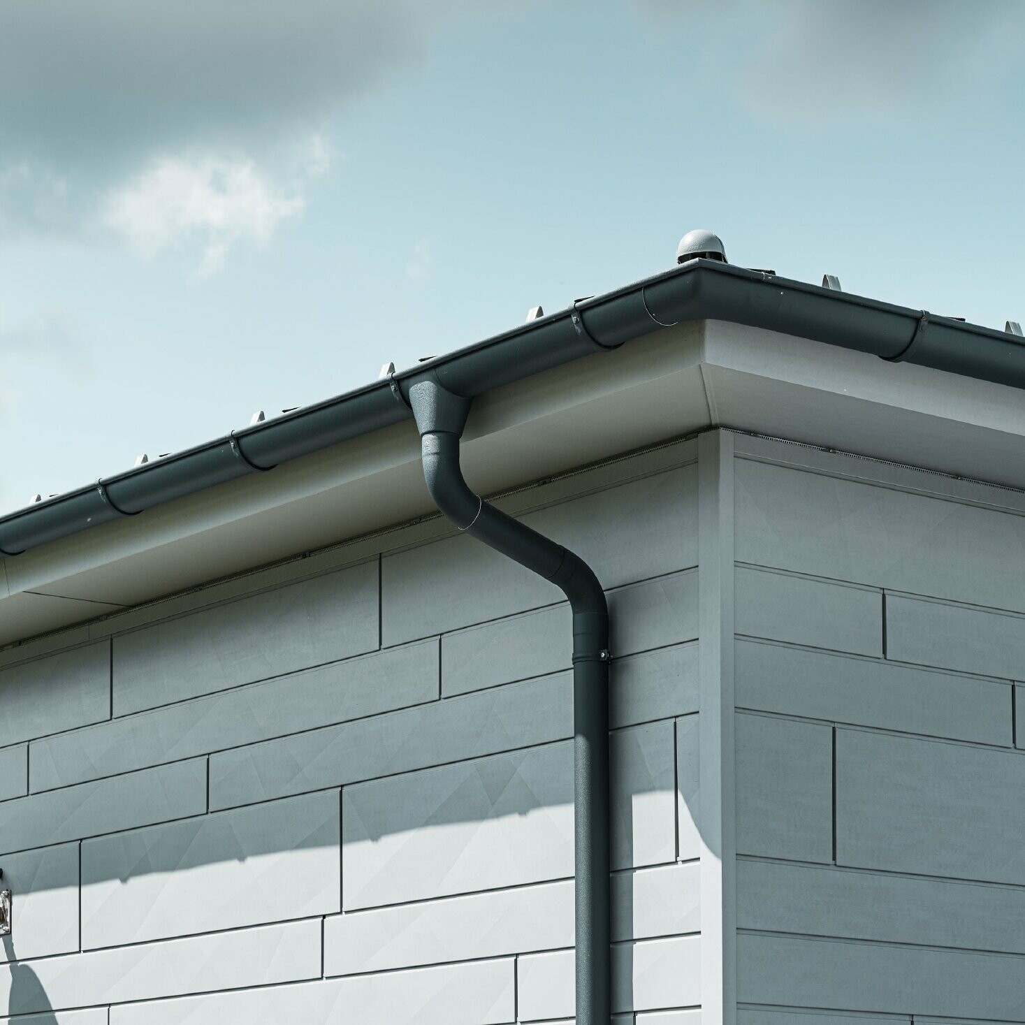 Suprafață inferioară a acoperișului cu jgheab PREFA, jgheaburi și burlan în antracit cu PREFA Siding.X Fațadă în gri patinat