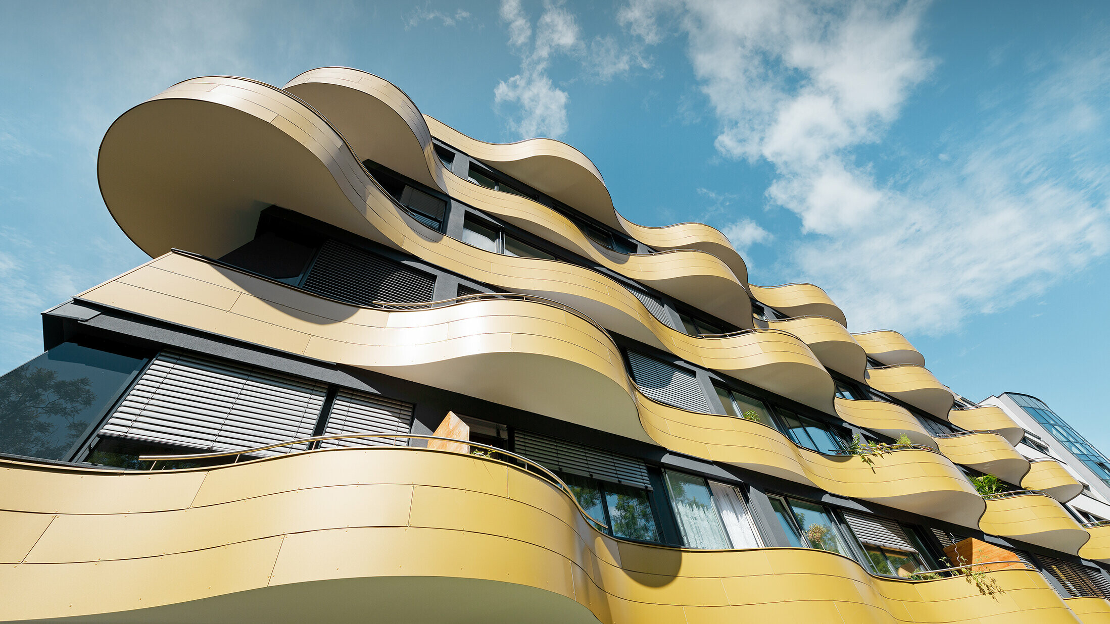 Froschperspektive auf die einzigartige Fassadengestaltung der Wohnhausanlage "Goldene Welle" in Graz. Die goldenen Balkone mit ihren speziellen Rundungen wurden mit Aluminium Verbundplatten bekleidet.