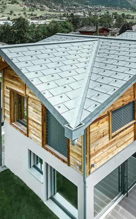 Vilă în stil elvețian cu un acoperiș din aluminiu de la PREFA. S-a montat element classic R.16 în culoarea gri piatră. La etajul superior s-a montat o fațadă din lemn rustică.