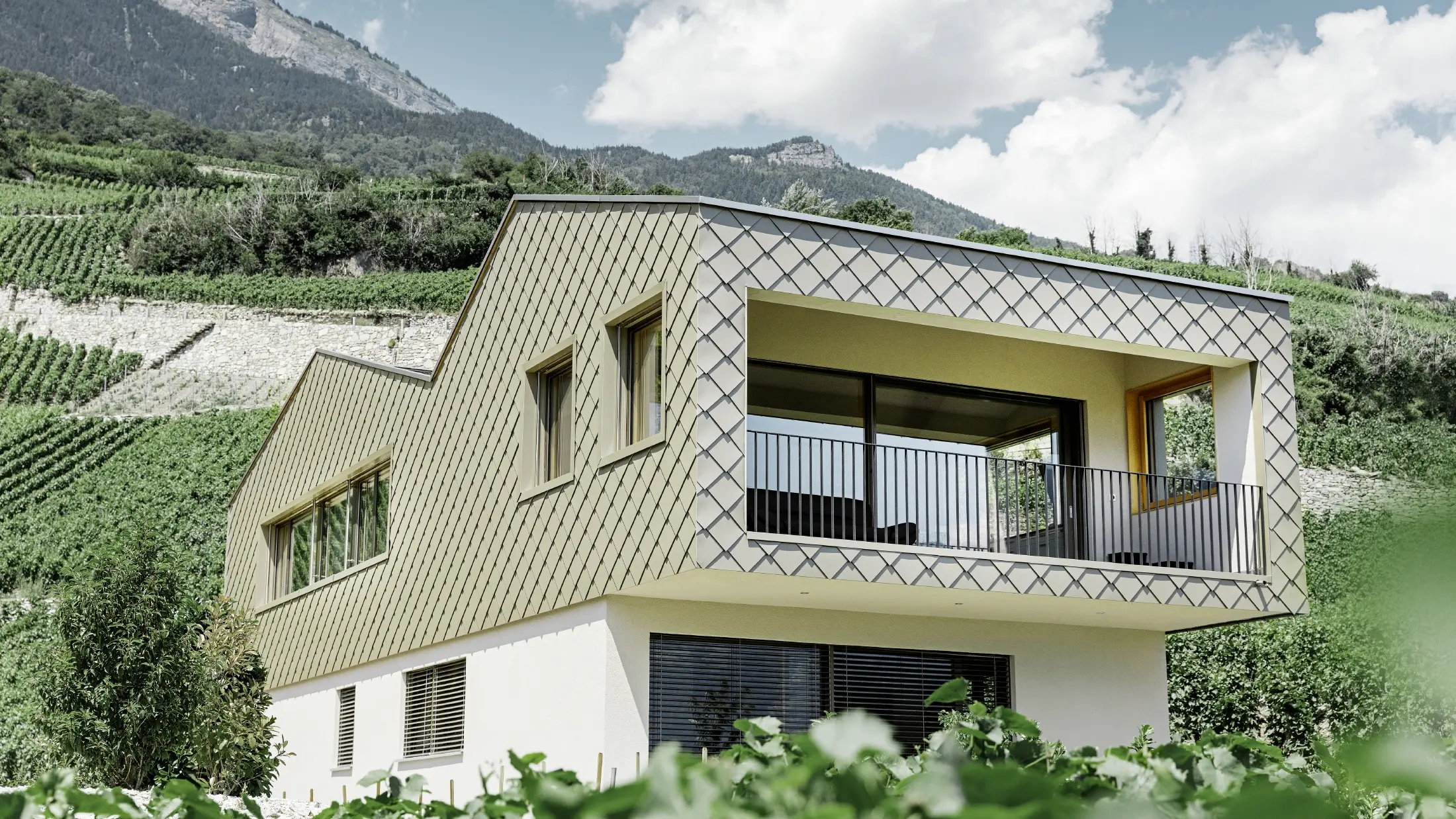 casă monofamilială modernă în viile din Valea Rhônului cu 4 suprafețe de acoperiș diferite și galerie deschisă cu fațadă cu solzi în culoarea bronz