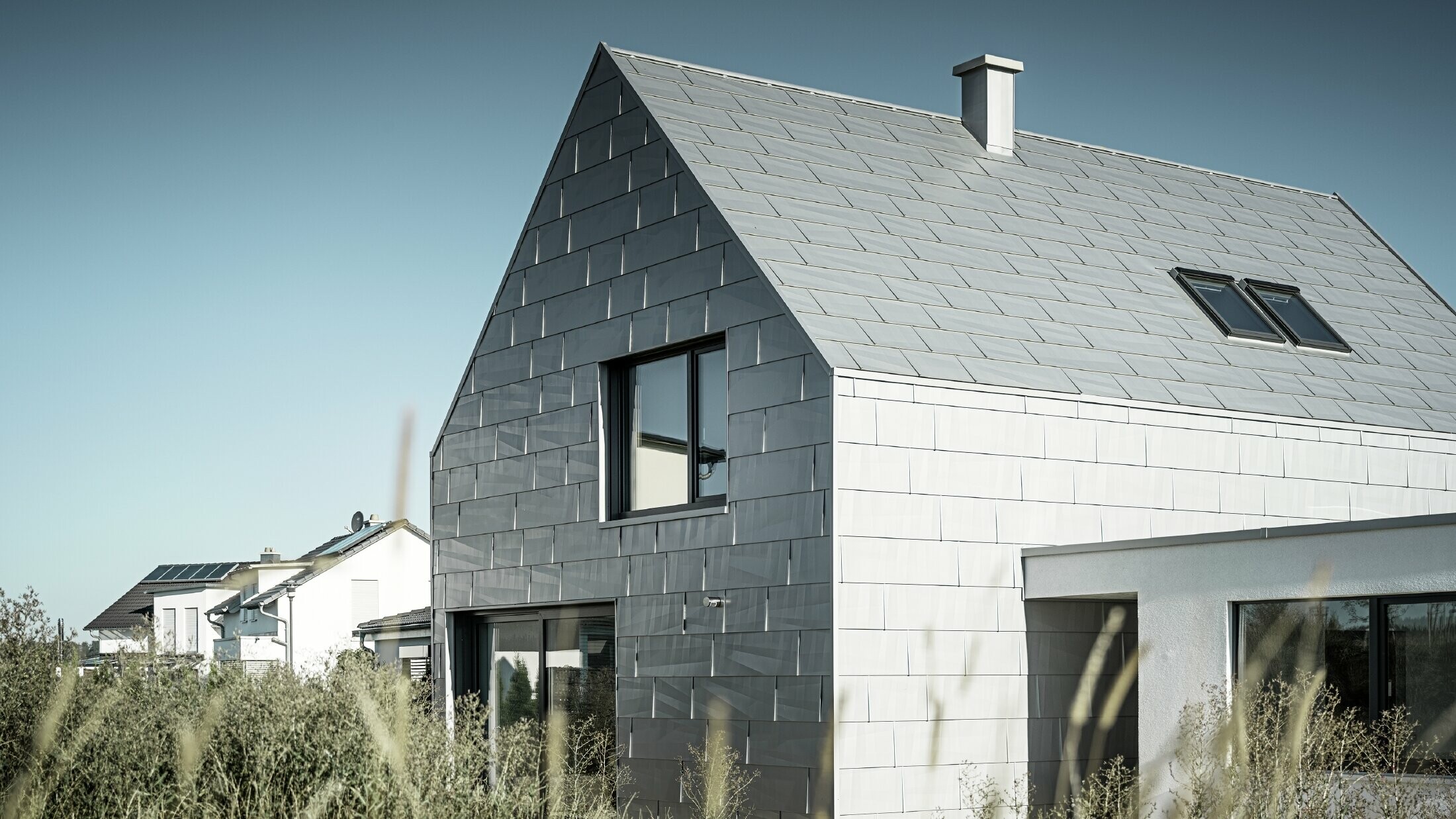 Clădirea de birouri din perspectivă laterală, acoperită complet cu produsul pentru acoperișuri și fațade FX.12 PREFA în culoarea P.10 argintiu metalic. 