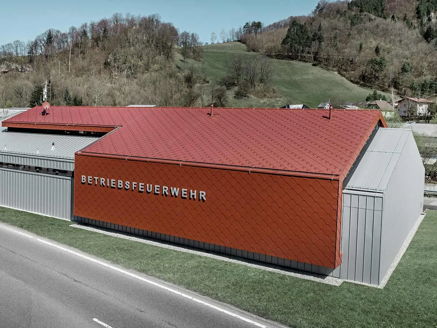 Noul sediu al pompierilor firmelor PREFA și Neuman Aluminium a fost placat cu noii solzi romboidali pentru acoperiș și fațadă 44 × 44 în culoarea P.10 roșu oxid, precum și Prefalz în culoarea argintiu metalic.