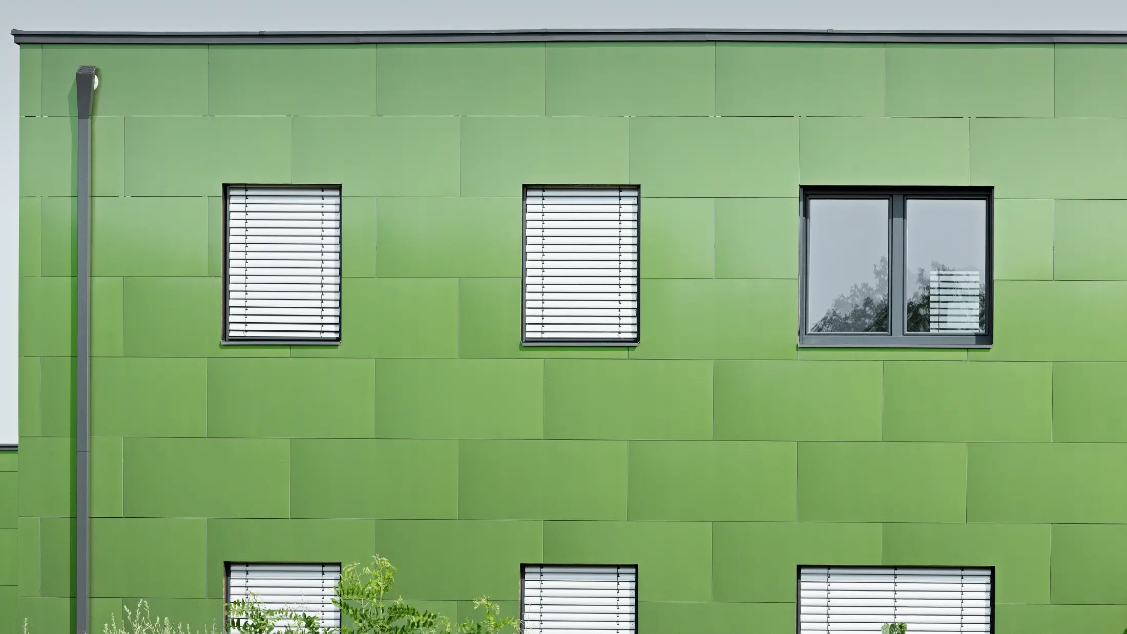 Vedere frontală a plăcii compozit din aluminiu PREFA cu aspect cameleon și colorit schimbător. În stânga se vede burlanul rectangular, burlanul dreptunghiular PREFA