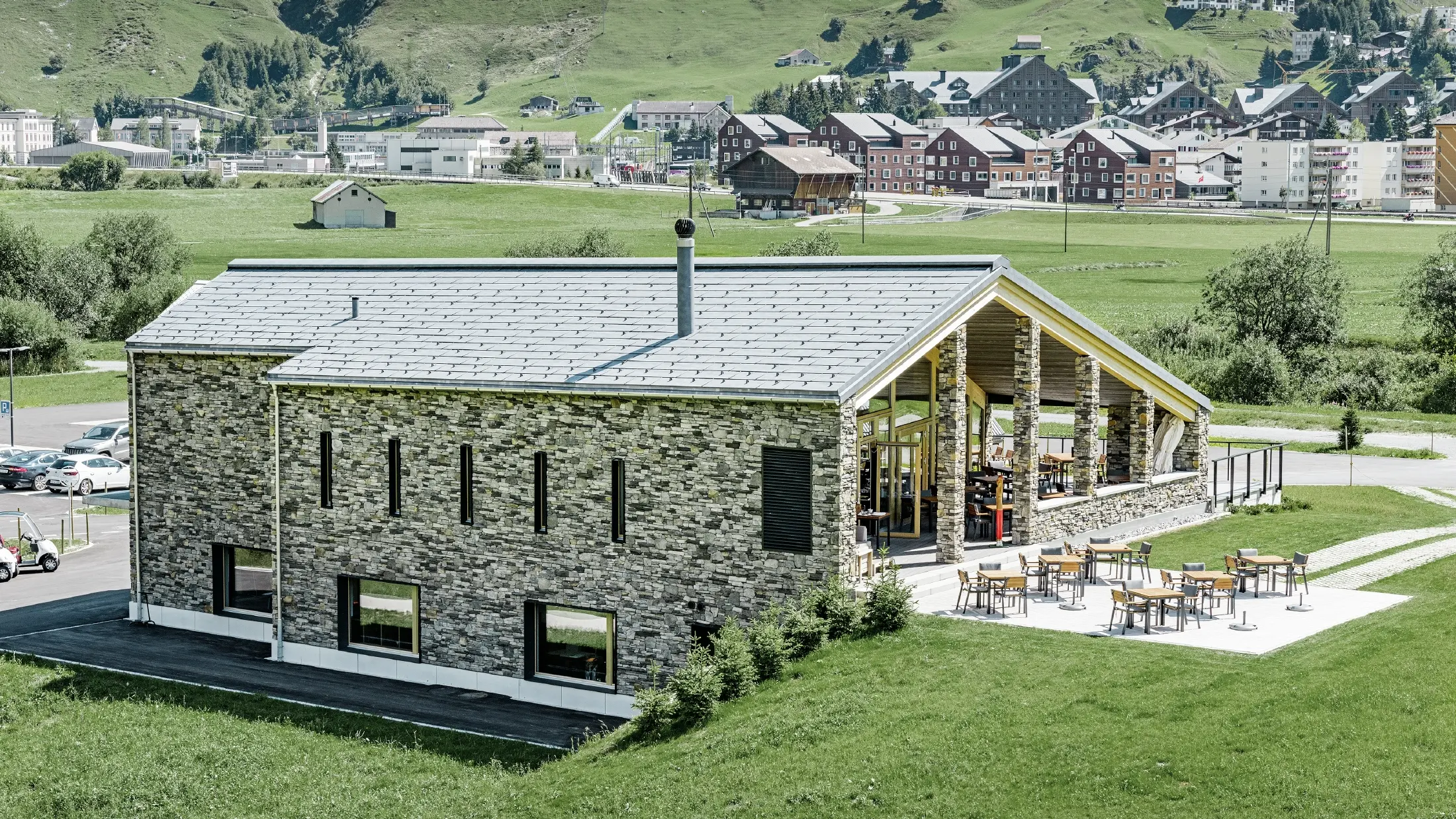 Clădire modernă de club a terenului de golf din Andermatt cu fațadă din piatră și panouri pentru acoperiș PREFA FX.12 din aluminiu în culoarea gri piatră