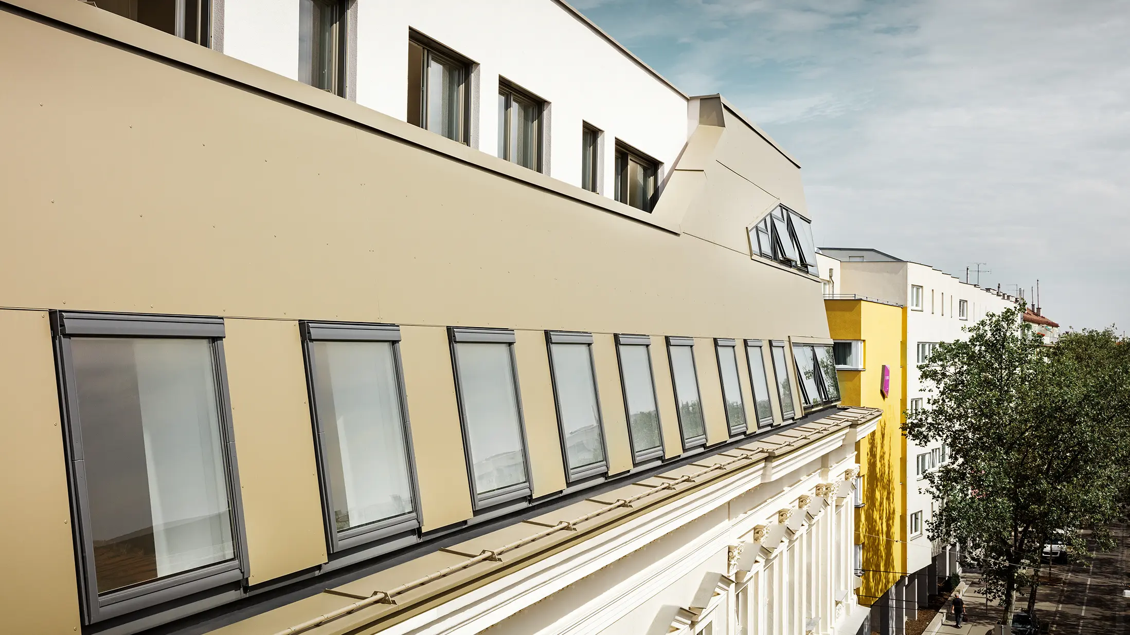 Vederea laterală a mansardei evidențiază placarea uniformă cu plăci compozit din aluminiu PREFA în culoarea bronz. Ferestrele mari și elementele vitrate de mari dimensiuni asigură încăperi inundate de lumină și un aspect elegant, modern.
