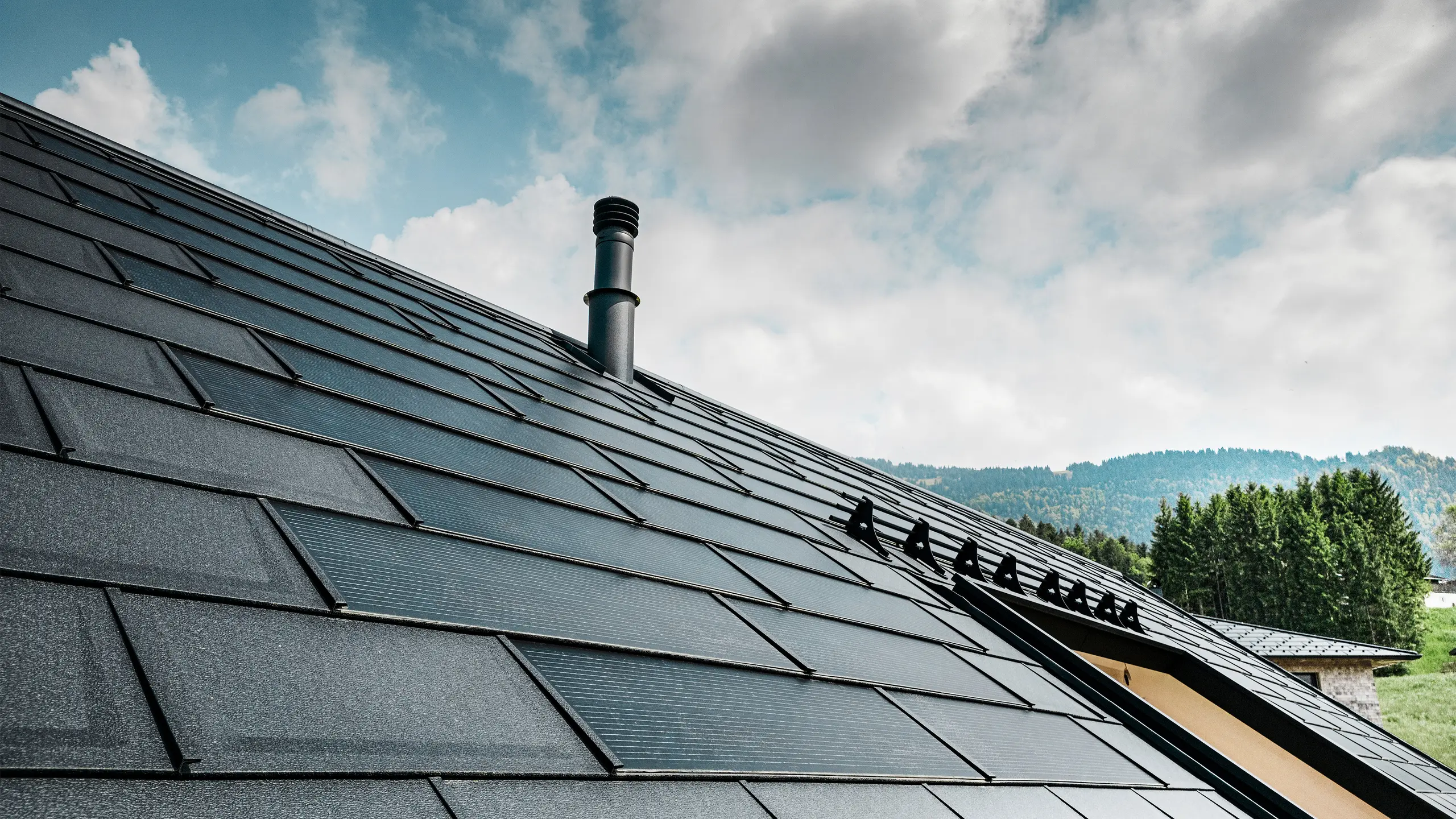 Vedere detaliată a panoului solar pentru acoperiș PREFA, combinat cu consacratul R.16 element classic PREFA în culoarea P.10 negru, pe o casă ecologică din Egg, Austria. Modulele fotovoltaice integrate demonstrează îmbinarea perfectă dintre energia regenerabilă și designul sofisticat al acoperișului. Elementele classic R.16 de culoare neagră, prevăzute cu sistem de protecție împotriva zăpezii, completează aspectul estetic al acoperișului și asigură totodată siguranța.
