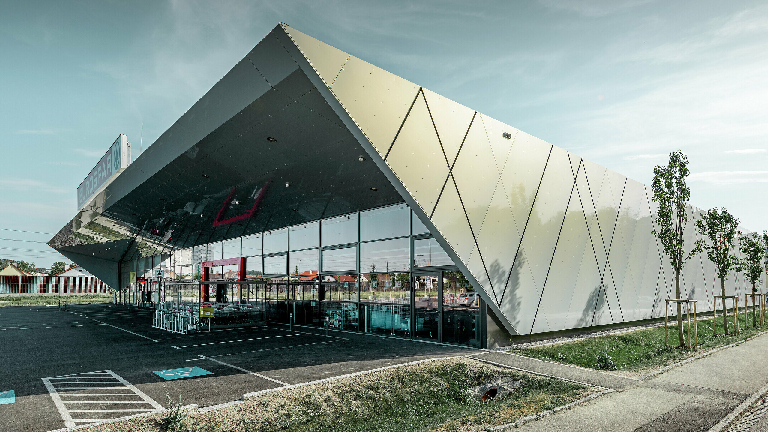Der Eingangsbereich des EUROSPAR Supermarkts kombiniert großzügige Glasflächen mit einer markanten PREFA Aluminiumfassade. Die glänzende Oberfläche der Sonderfarbe Silver Gold unterstreicht die hochwertige, zukunftsorientierte Architektur der Supermarktfiliale. Die Aluminium Verbundplatten schillern in der Sonne je nach Blickwinkel in unterschiedlichen Farben.