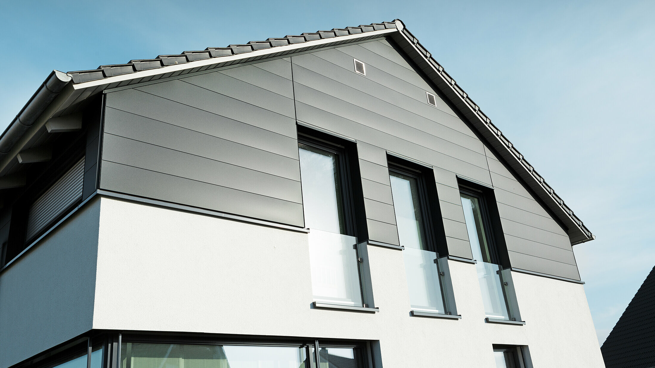 Fațadă modernă de casă în Isenbüttel cu PREFA Sidings în P.10 antracit – placarea din aluminiu conferă casei monofamiliale un aspect elegant și rezistent la intemperii. Ferestrele verticale accentuează suplimentar arhitectura modernă.