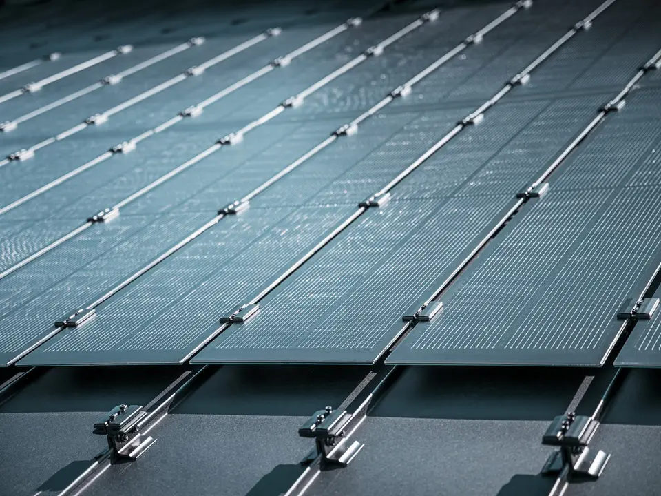 Montageansicht mehrerer PREFALZ Solarmodule auf einem bestehenden PREFALZ Dach in Meschede, Deutschland. Die rahmenlosen Glas/Glas-PV-Module sind in präzisen Reihen angeordnet und mit robusten Halterungen fixiert, was eine flächenbündige, elegante Optik erzeugt. Die hochwertige Befestigungstechnik sorgt für Stabilität und Langlebigkeit, während die innovative TOPCon-Zellentechnologie maximale Energieeffizienz garantiert. Das Bild vermittelt modernste Photovoltaik-Lösung, die Design, Funktionalität und Nachhaltigkeit perfekt vereint.