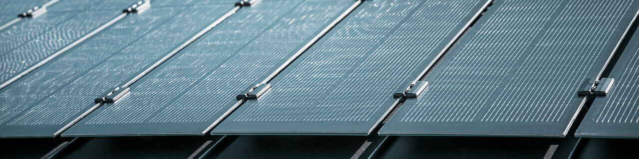 Montageansicht mehrerer PREFALZ Solarmodule auf einem bestehenden PREFALZ Dach in Meschede, Deutschland. Die rahmenlosen Glas/Glas-PV-Module sind in präzisen Reihen angeordnet und mit robusten Halterungen fixiert, was eine flächenbündige, elegante Optik erzeugt. Die hochwertige Befestigungstechnik sorgt für Stabilität und Langlebigkeit, während die innovative TOPCon-Zellentechnologie maximale Energieeffizienz garantiert. Das Bild vermittelt modernste Photovoltaik-Lösung, die Design, Funktionalität und Nachhaltigkeit perfekt vereint.