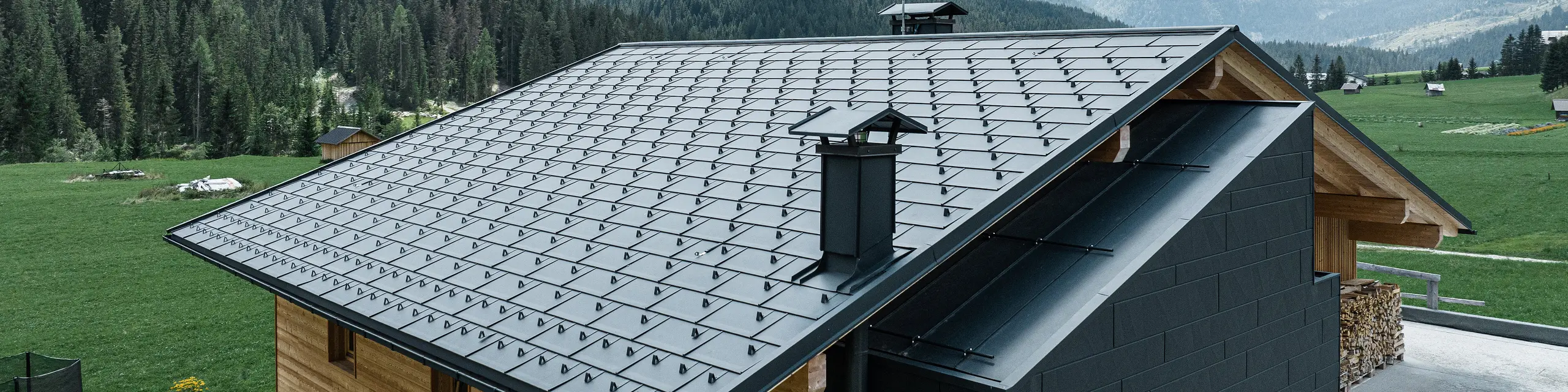Einfamilienhaus in Südtirol mit der PREFA Dachplatte R.16 in der Farbe P.10 Schwarz. Ein Teil der Fassade ist mit PREFA Siding.X bekleidet. Im Hintergrund sieht man die Berglandschaft.