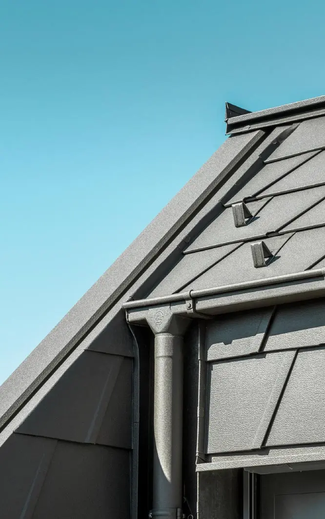 Dach mit PREFA Aluminiumdachplatten und modernen Regenrinnen, die eine hohe Langlebigkeit und ästhetische Funktionalität bieten, vor einem klaren blauen Himmel.