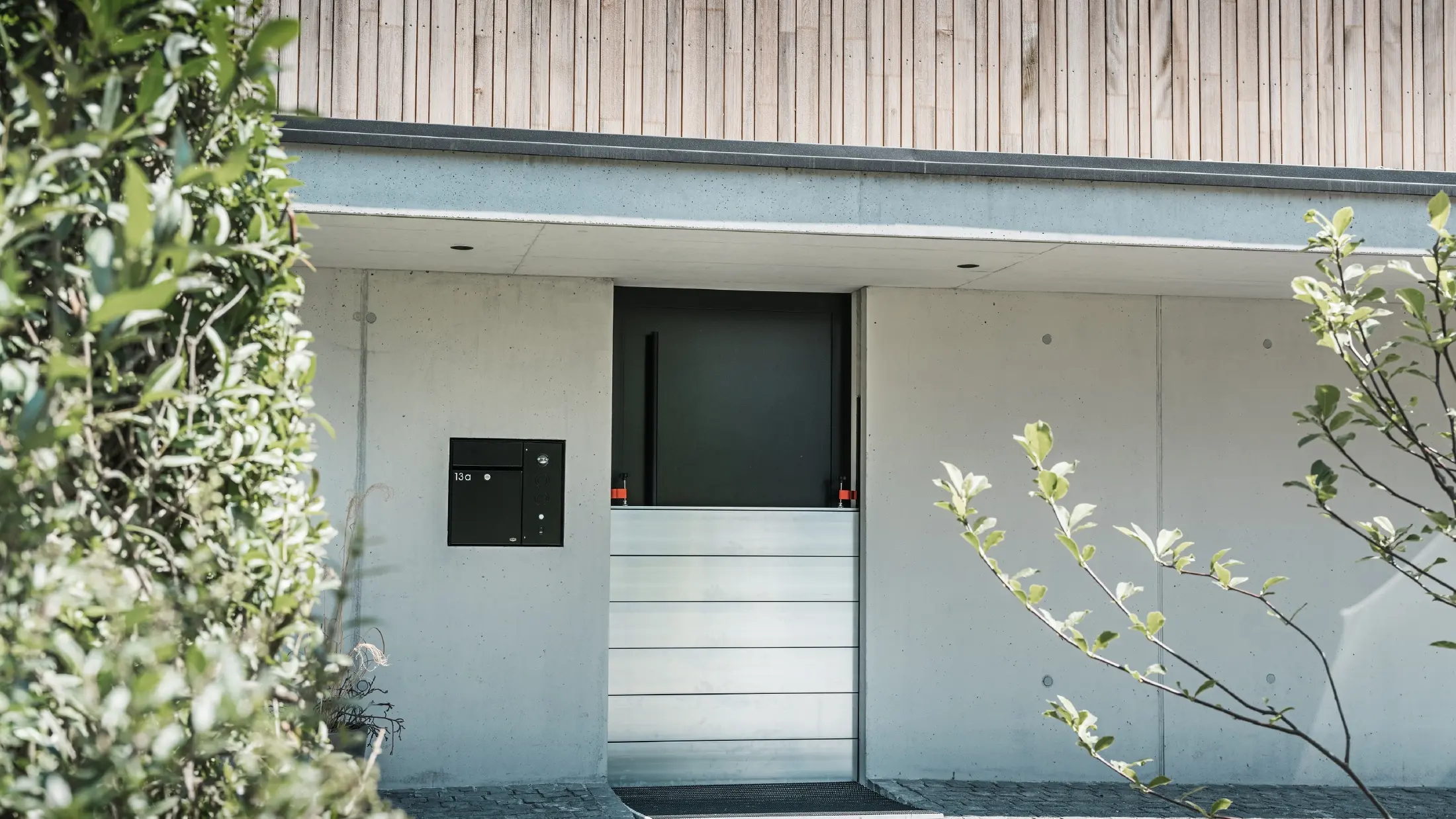 Vor der Eingangstür eines Einfamilienhauses mit Holzfassade wurde der PREFA Hochwasserschutz montiert. Die robusten Dammbalken aus Aluminium garantieren langfristige Sicherheit gegen Hochwasser und Schlamm.