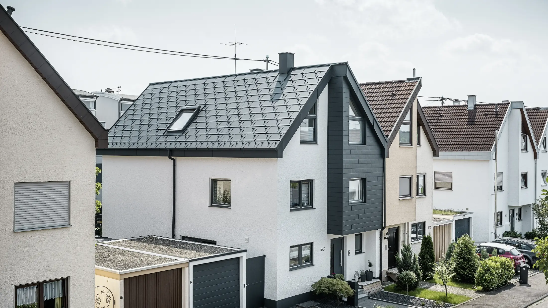 O jumătate de duplex a fost deja renovată, cu fațadă proaspăt tencuită, albă, combinată cu o fațadă PREFA Siding.X în culoarea antracit. Acoperișul a fost învelit cu element classic PREFA R.16. Sistemul pluvial este realizat din jgheab dreptunghiular inclusiv burlan PREFA.