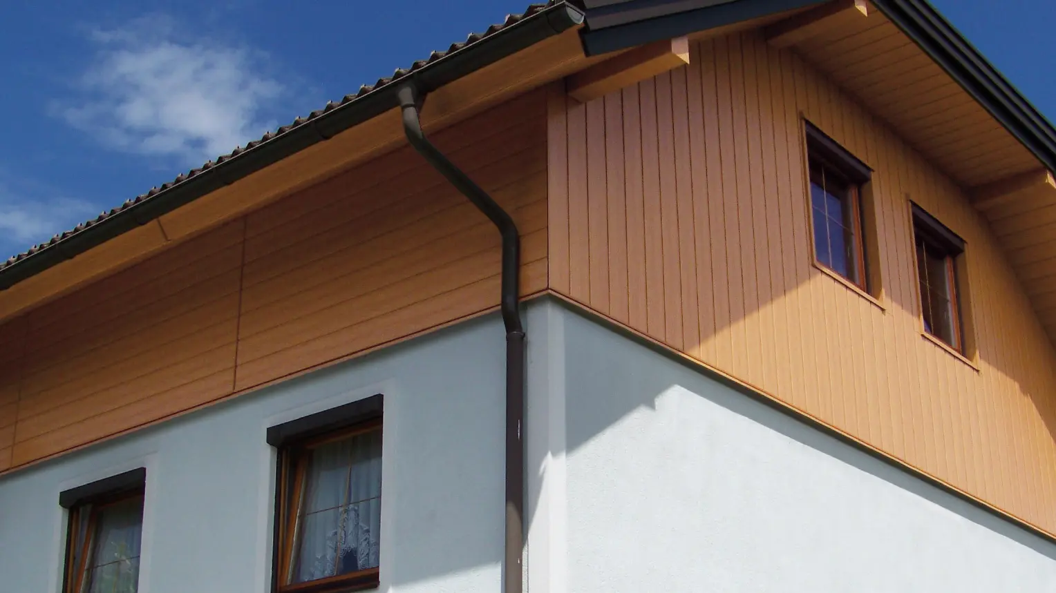 Casă monofamilială mari cu acoperiș cu pantă frântă și fronton placat cu panourile de fațadă PREFA cu aspect de lemn (culoare stejar natur)