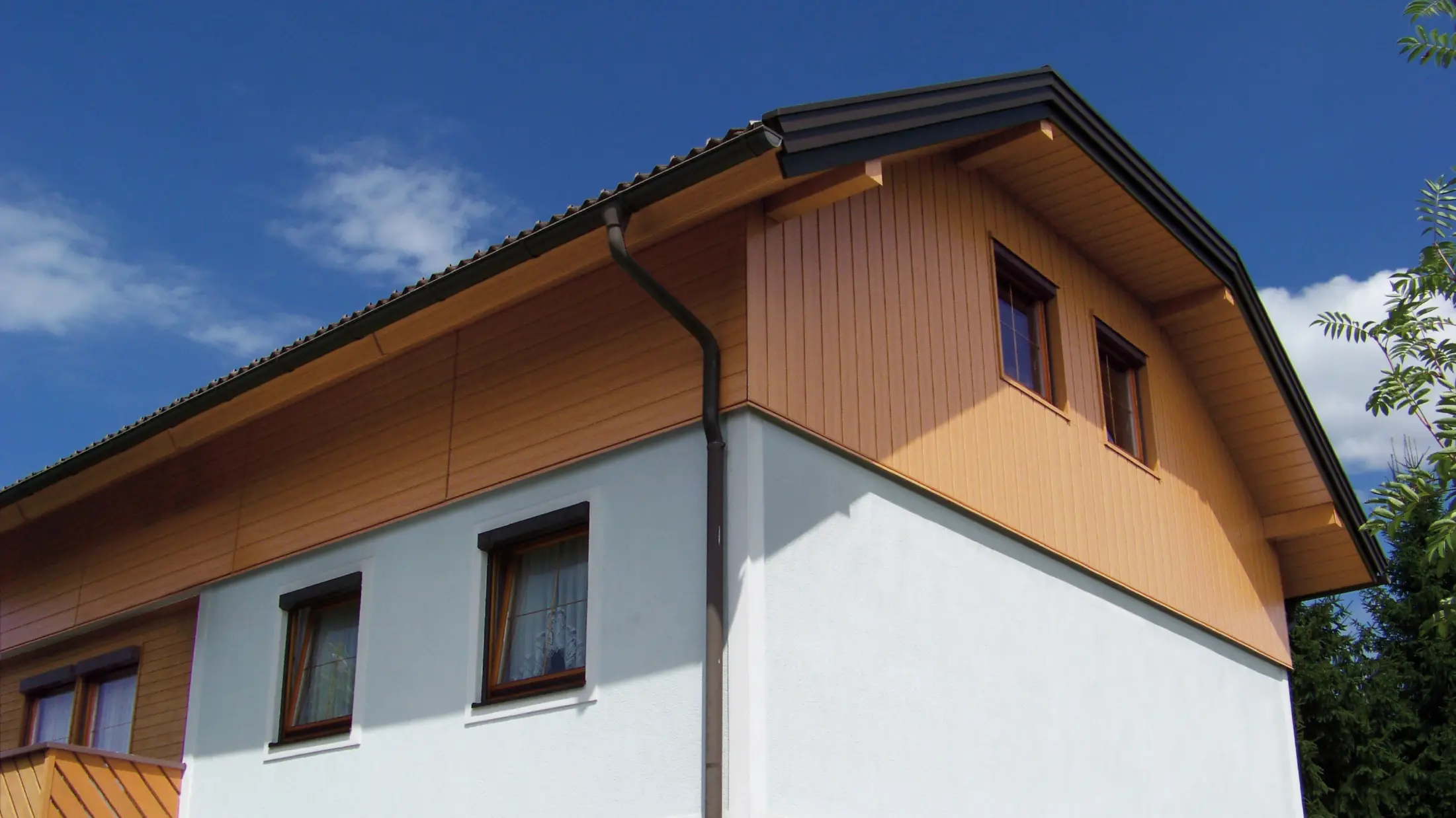 Casă unifamilialăcu acoperiș cu ruptură de pantă și fronton placat cu panourile de fațadă PREFA Sidings cu aspect imitație lemn (culoare stejar natur)